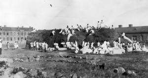 Children climbing on an enormous pile of straw in the Alexandropol courtyard. Some of the boys are unloading straw from white bags.