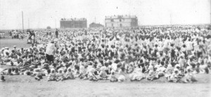 Large group of children on the grounds of the Alexandropol orphanage complex. Two large orphanage buildings are visible in the background.
