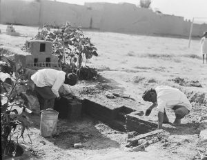 Two boys build a mud brick wall in front of their small playhouse in the orphanage yard.
